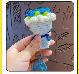 Detailed close-up of a handmade blue crochet flower bouquet keychain with white lace wrap