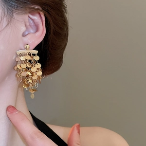 Close-up of golden multi-layer metal disc tassel earrings worn by a model in soft light
