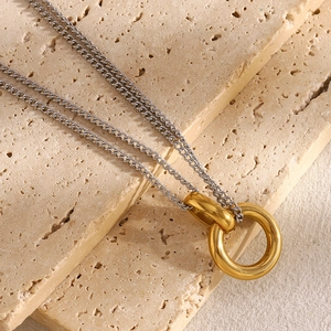 Detail of a minimalist double-chain necklace with a gold ring pendant on textured stone