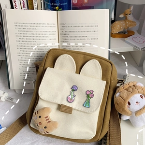 Cute canvas crossbody bag with cat plush pendant and floral badges on a desk setup