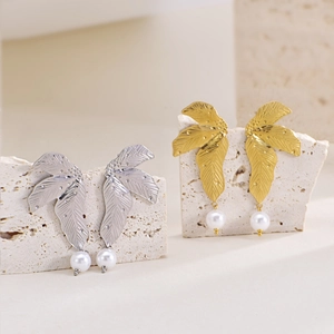 Close-up of irregular leaf earrings with white pearls on a textured stone surface