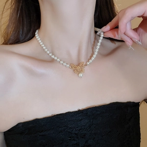 Vue détaillée du pendentif papillon doré ajouré et de la perle goutte sur le collier choker