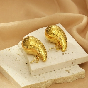 Golden hollow teardrop earrings with textured hammered finish on white stone