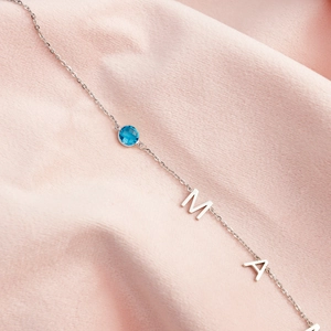 Silver stainless steel MAMA necklace featuring a round blue gemstone on a pink fabric background