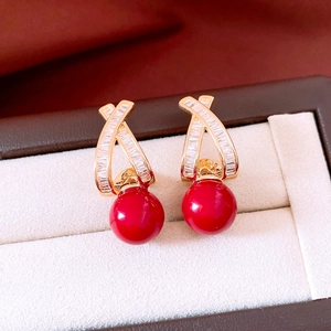 Detailed view of 18k gold plated earrings with zircon X-shape and red pearl drops