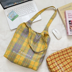 Detailed flat lay of a yellow and purple plaid canvas tote bag with embroidery text