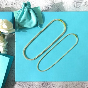 Detailed macro view of two golden sparkling zircon tennis chains on a teal background
