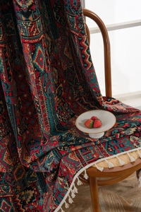 Detail of bohemian woven blanket with geometric patterns and white fringe on a chair