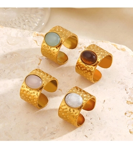 Detailed view of four hammered gold rings with oval gemstones on a stone base