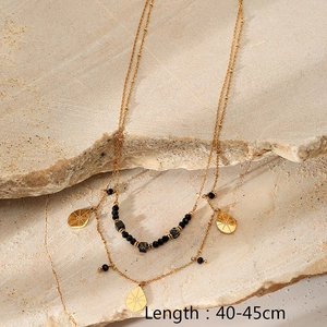 Detail of double-layer gold necklace with black beads and teardrop pendant on stone