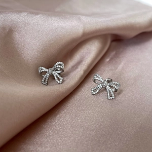 Detail of silver S925 bow earrings with sparkling pave-set diamonds on silk fabric