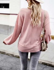 Detail of pink waffle knit sweater featuring a long sleeve design and a curved hemline