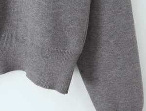 Detailed close-up of the ribbed hem and cuffs on the grey knitted three-piece set