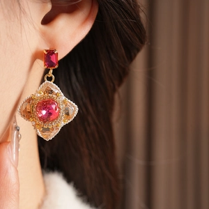 Close-up of vintage diamond-shaped earrings with red gemstone and pearls on a model