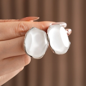 Detail shot of irregular silver earrings with glossy white inlay held between fingers