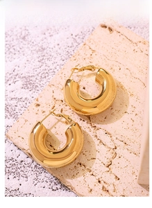 Detailed view of polished gold U-shape chunky earrings on textured stone surface