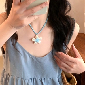 Détail du collier de perles en céramique bleue avec pendentif fleur en coquillage