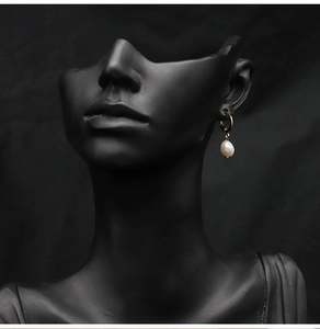 Detailed view of elegant gold hoop earring with white drop pearl on a dark mannequin