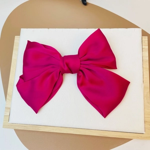 Macro detail of magenta satin bow hair clip showing smooth texture and premium glossy finish