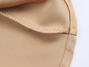 Detailed macro view of beige sequin fabric texture with precise overlock stitching on the hem