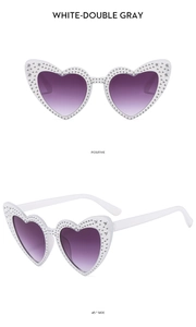Detail view of heart-shaped sunglasses with white frame, purple lenses, and rhinestones