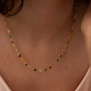 Close-up of gold necklace featuring small square multi-colored zircon stones on model