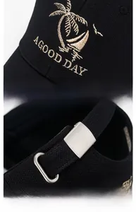 Detail showing palm tree embroidery and adjustable silver metal buckle on black baseball cap
