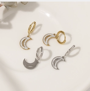 Close-up of gold and silver moon earrings with zircon inlay on a white porcelain dish