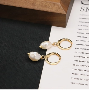 Detailed shot of baroque irregular pearl earrings with golden hoop clasp on a wooden display