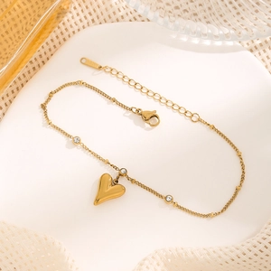 Detailed macro of gold-tone heart anklet with zircon on a clean white stone base