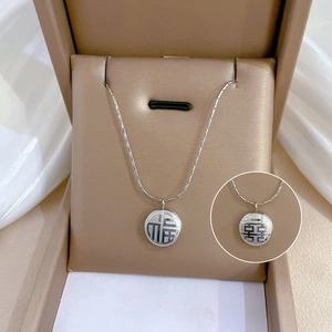 Détail du collier en acier titane avec pendentifs Fu et Xi dans un écrin à bijoux