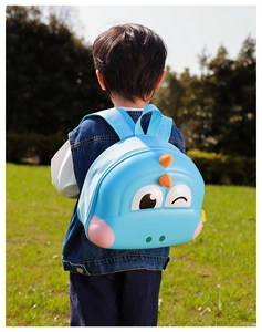 Rear view of a child wearing a blue dinosaur hardshell backpack in a sunny park