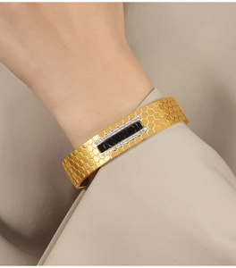 Detail of a gold honeycomb textured bangle with black rectangle gems and white zircons