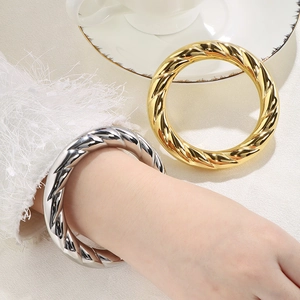 Detailed view of thick twisted spiral bangles in polished 18k gold and silver steel finish