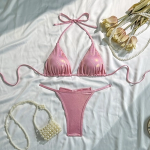 Flat lay of pink glitter bikini with pearl accessories on white silk background