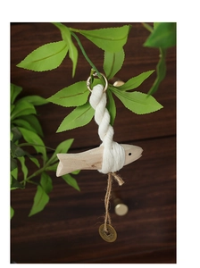 Detail of wooden fish ornament with woven rope and antique coin on a dark background