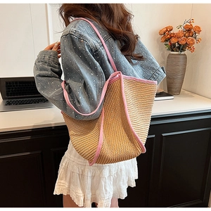 Detail of hand-woven straw tote bag with pink contrast fabric trim on a model's shoulder