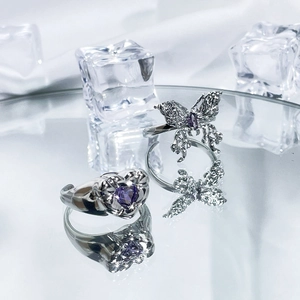 Silver butterfly and heart rings with purple gemstones on reflective icy surface