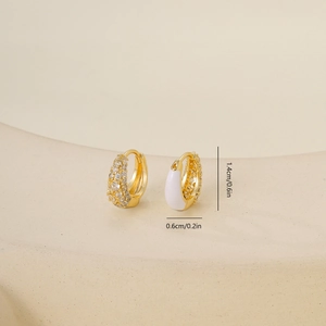 Macro view of gold huggie earrings with cubic zirconia and white enamel details