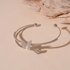 Macro detail of silver-tone zircon butterfly and clover accents on a layered open bangle