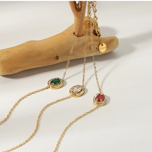 Detailed view of three gold titanium steel necklaces with emerald, ruby, and clear gemstones
