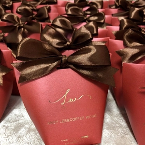 Multiple red paper wedding gift boxes with gold foil text and brown satin ribbon bows