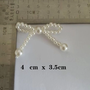 Macro detail of pearl bow accessory with scale showing dimensions 4cm x 3.5cm