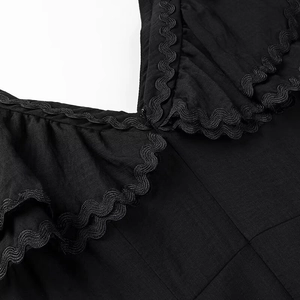Dettaglio di un abito nero con maniche a balze e finiture decorative in nastro ondulato