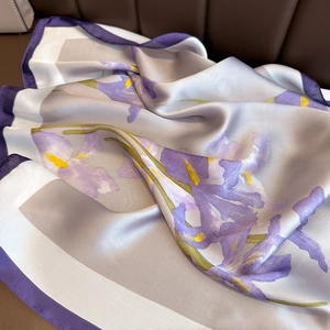 Purple floral silk scarf with iris patterns and yellow accents on brown leather surface