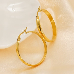 Detailed close-up of large polished gold hoop earrings on elegant silk fabric