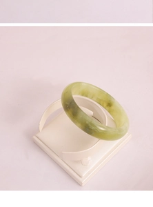 Macro shot of light green jade bangle displayed on a white professional jewelry rack