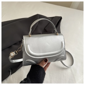 Macro detail of silver flap bag featuring unique U-shaped stitching and gold-tone hardware