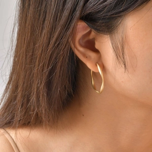 Detail of matte gold twisted C-shaped earring on model showing minimalist metal texture