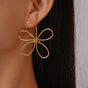 Detail view of large gold hollow flower earrings with twisted metal wire lines on model